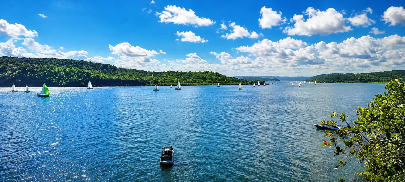 Baía de águas calmas com barcos e mata ao fundo